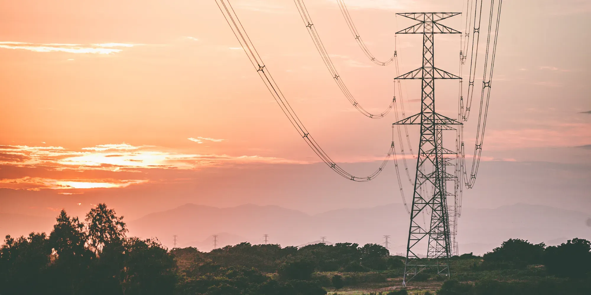 Tall electricity transmission towers and power lines at sunset.