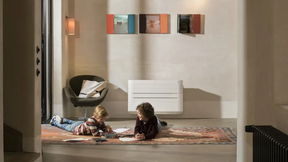 Two children playing on the floor in a living room with a wall-mounted heat pump in the background