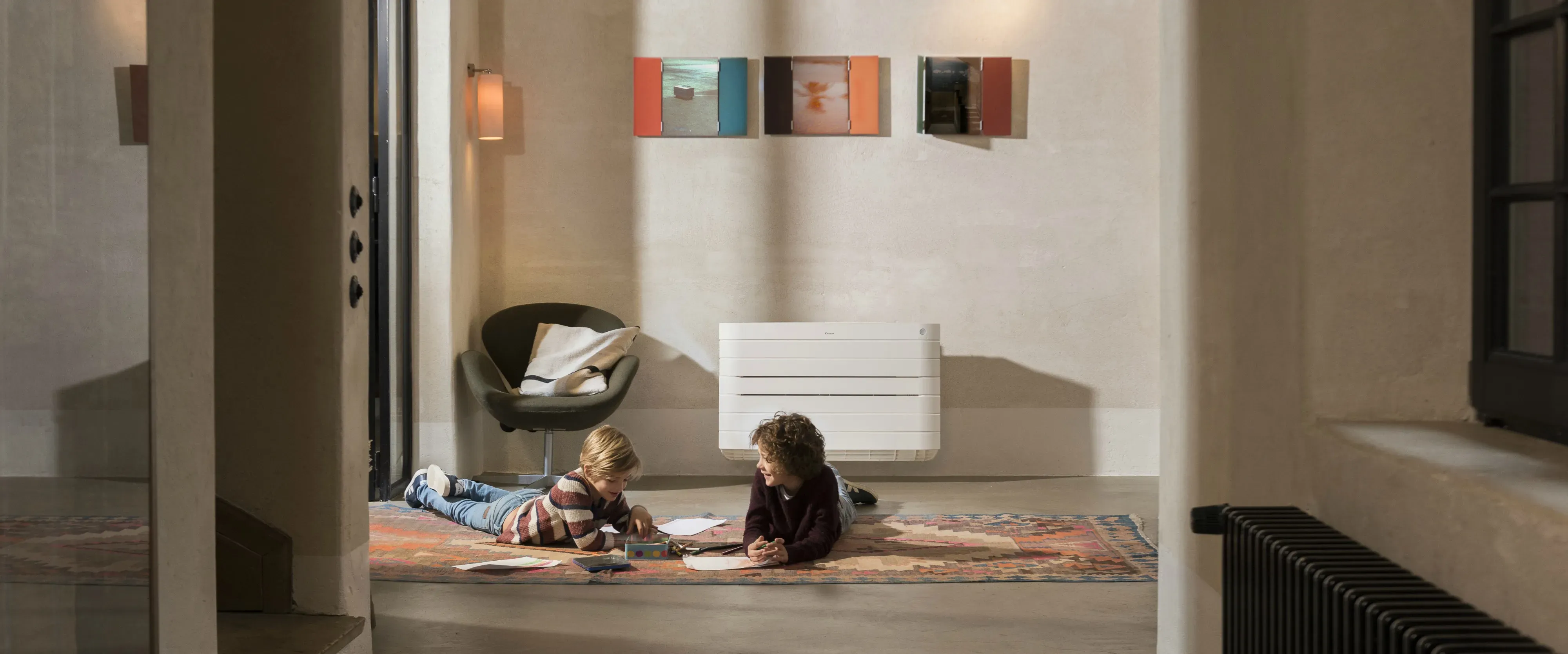 Two children playing on the floor in a living room with a wall-mounted heat pump in the background