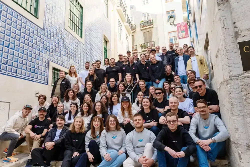 Team Nettbureau - Large group of people posing together in a narrow cobblestone alley.