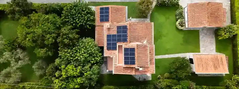 Vista aerea di una casa con tetto in tegole e pannelli solari, circondata da alberi e giardino.