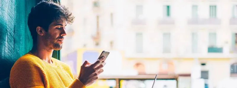 Mand sidder med sin mobiltelefon og computer.