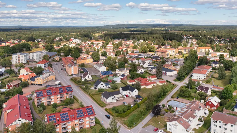 En stadsvy med hus, lägenheter och en bilväg, omgiven av grönska.
