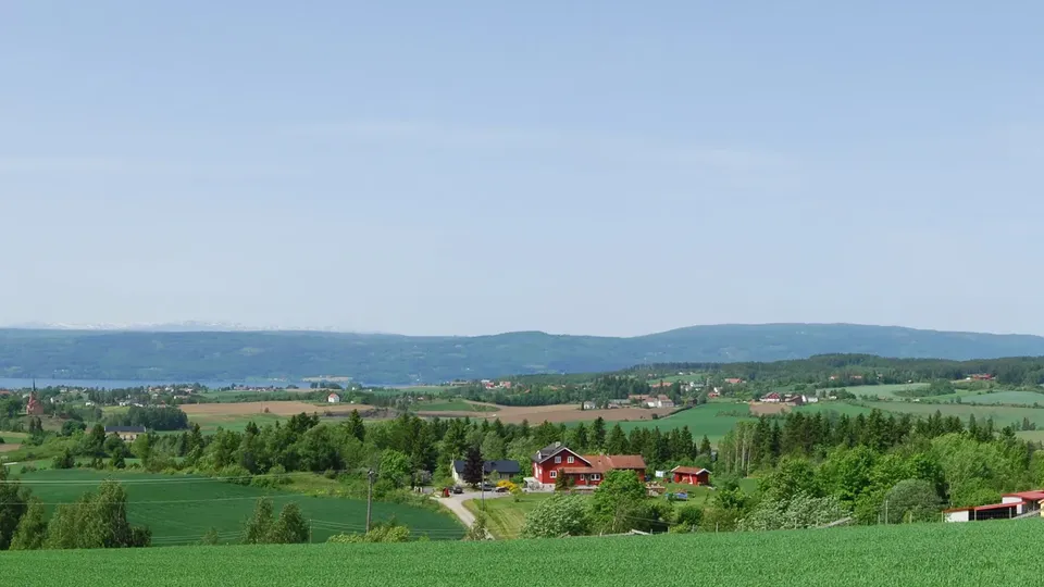 Panoramautsikt over et jordbrukslandskap med hus og åser i det fjerne.