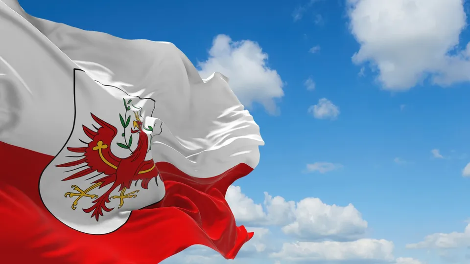 Rot-weiße Flagge Tirols mit dem Tiroler Wappen vor blauem Himmel mit Wolken.