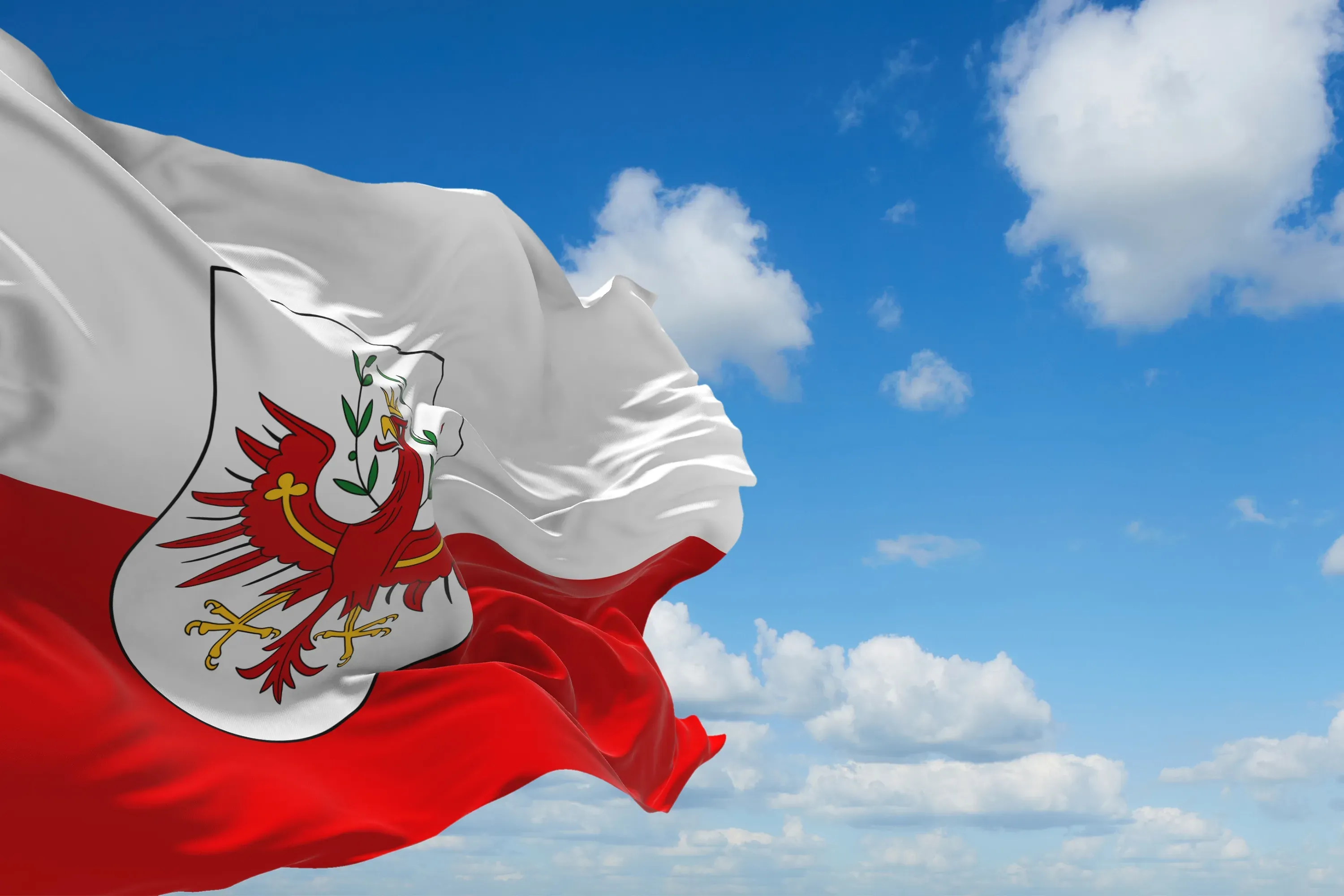 Rot-weiße Flagge Tirols mit dem Tiroler Wappen vor blauem Himmel mit Wolken.