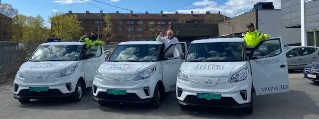 Tre varebiler står på rad, og ved hver bil lener en person seg ut av frontdøra.