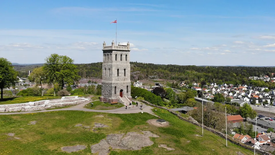 Slottsfjelltårnet som flagger og utsikt utover byen og skogslandskap.