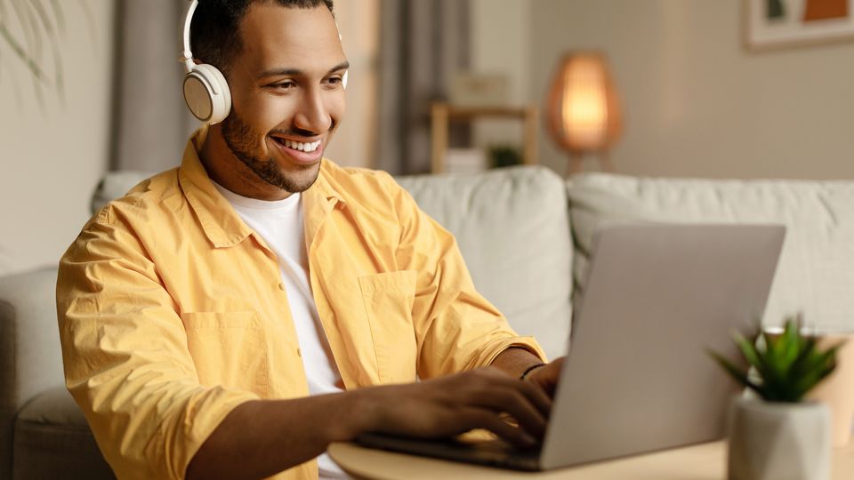 Bilde av en smilende mann med headset som sitter på en laptop.