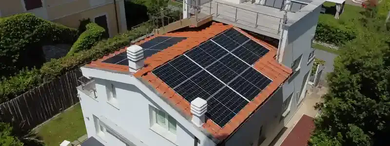 Vista aerea di una casa bianca con pannelli solari neri sul tetto in tegole di cotto, circondata da giardini.