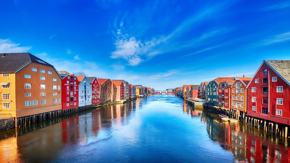 Fargerike bygninger ved vannkanten reflektert i blå elvekanal.
