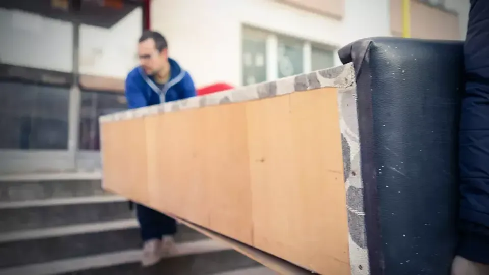 Två personer bär en stor kartongask genom en dörröppning.
