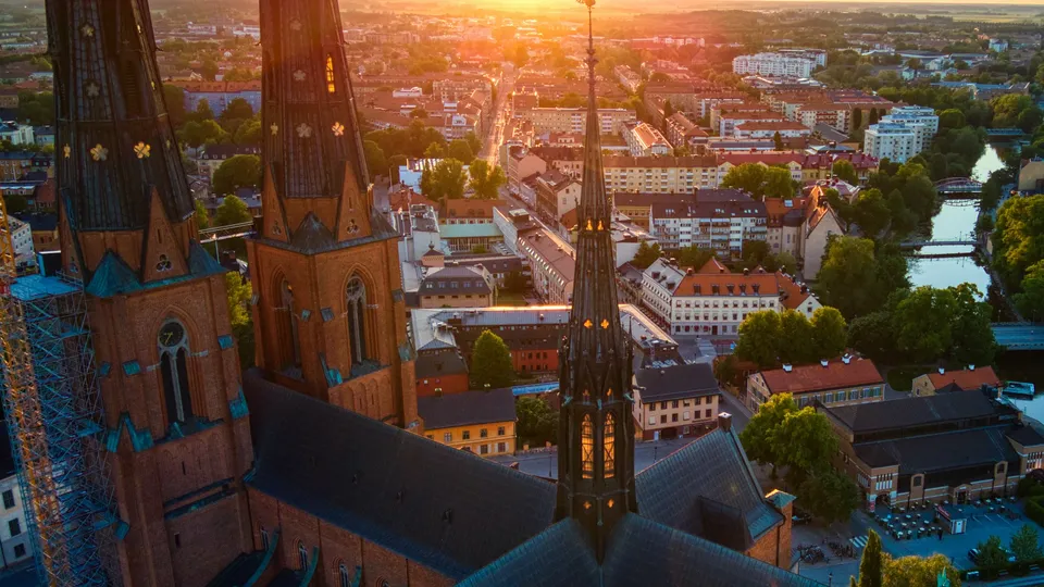Luftvy över tegeltornspiran på en Domkyrkan som överblickar Uppsala vid solnedgång.