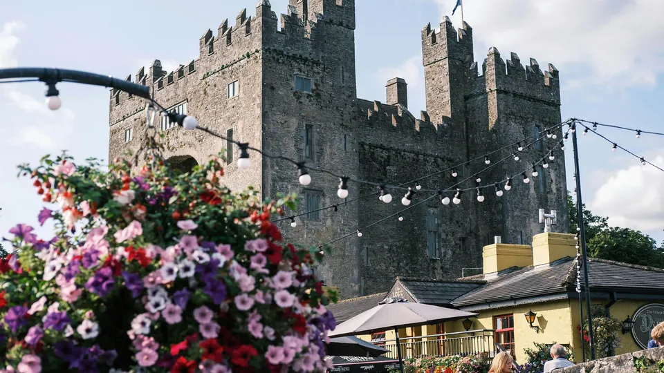 County Clare: Medieval stone castle with crenellated towers behind colorful flowers and outdoor venue.