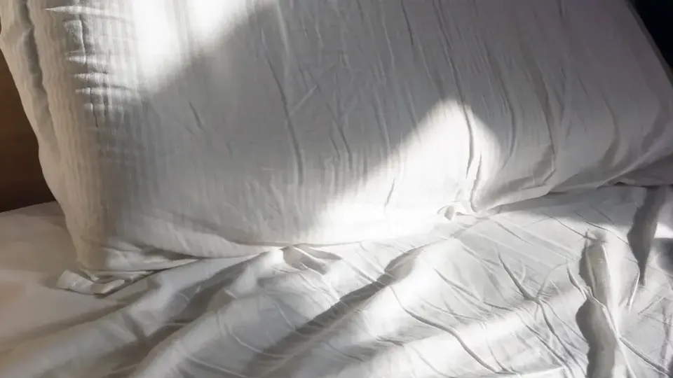 Vit bäddning med solljus som kastar skuggor över skrynkliga lakan.