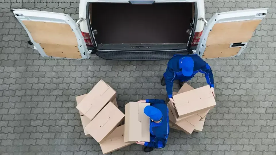 Två flyttarbetare packar in kartonger i en vit lastbil.