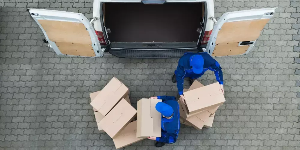 Två flyttarbetare packar in kartonger i en vit lastbil.