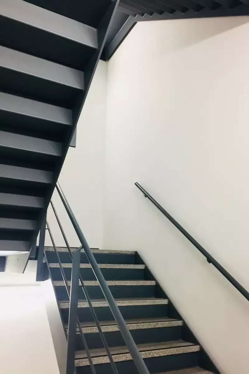 Svart metalltrappa med betongsteg och vita väggar.