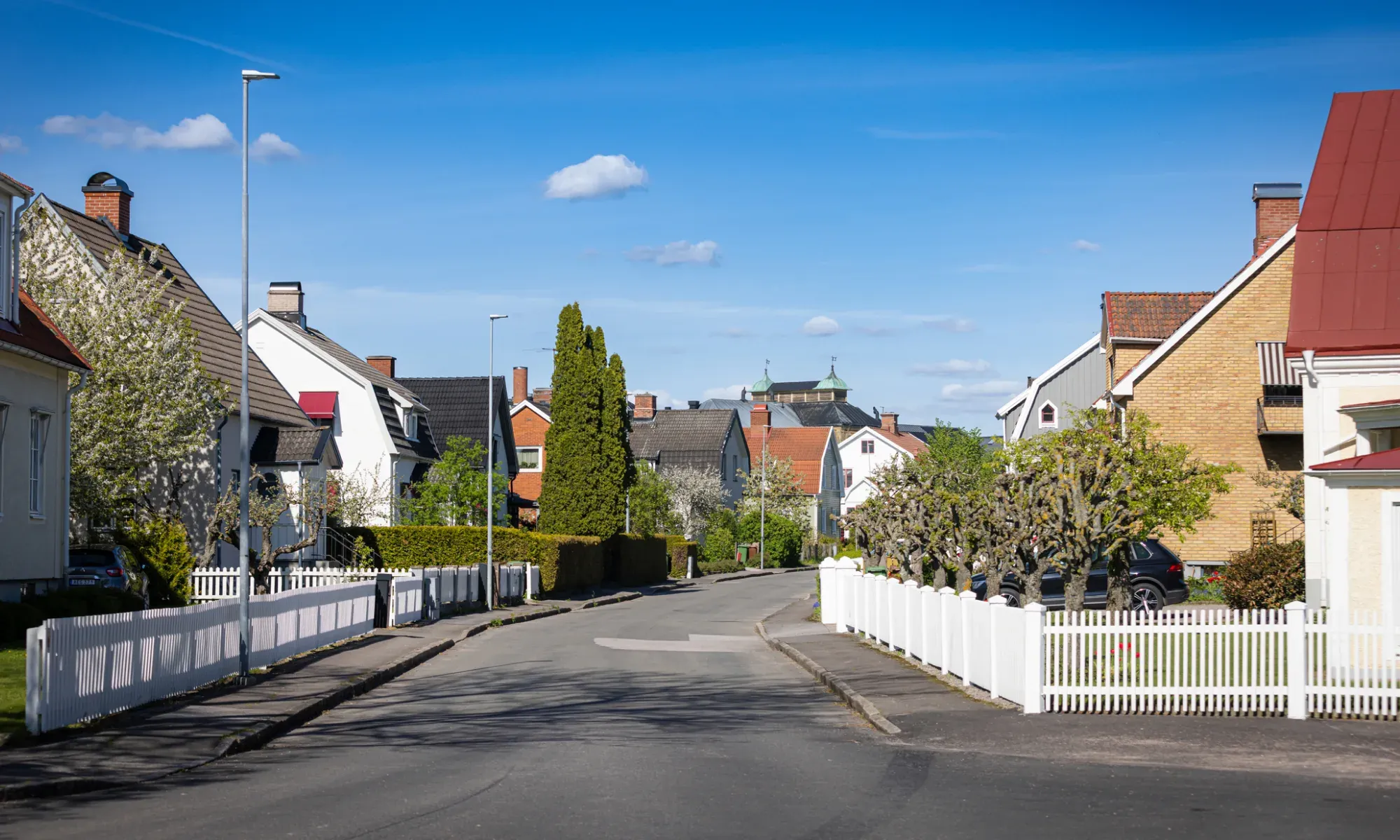 Lugn bostadsgata med vita staket och traditionella hus.