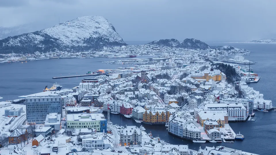 Snødekt kyst i Ålesund med havn og snøkledde fjell i bakgrunnen.
