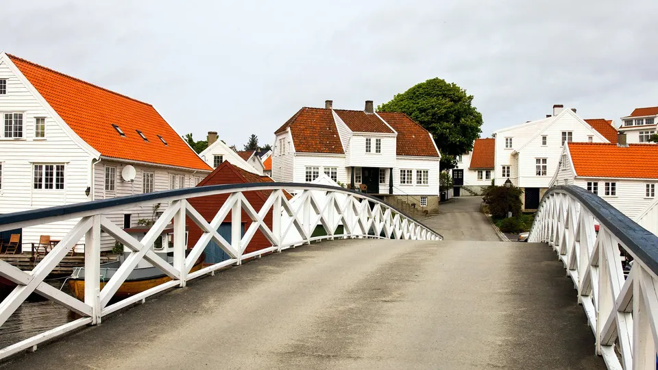 Hvit trebru som krysser mellom hvite hus med orange takstein i Karmøy.