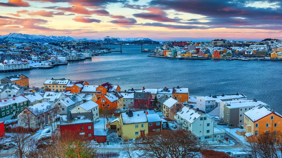 Fargerike hus på snøkledt bakke med utsikt over havn ved solnedgang.