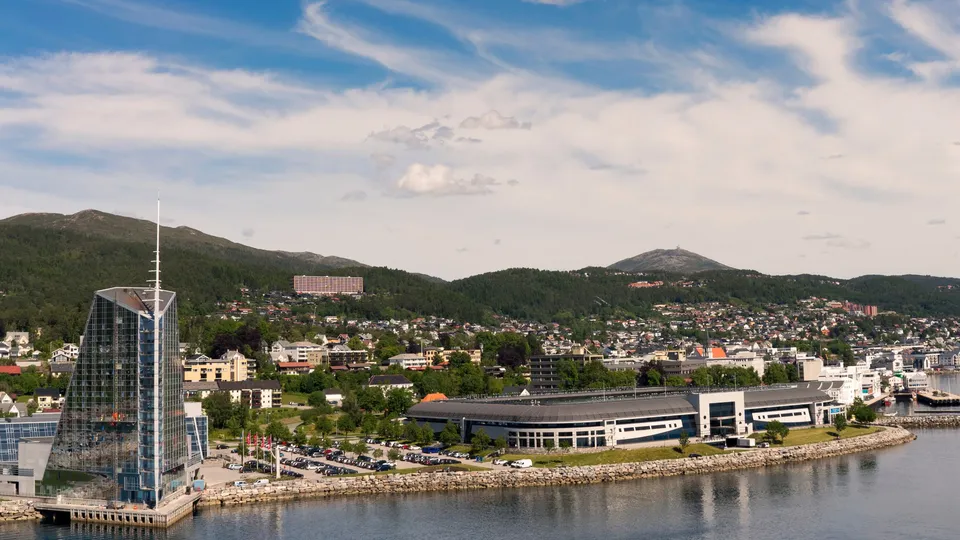 Byutsikt utover Molde med moderne bygning og skogkledde fjell.