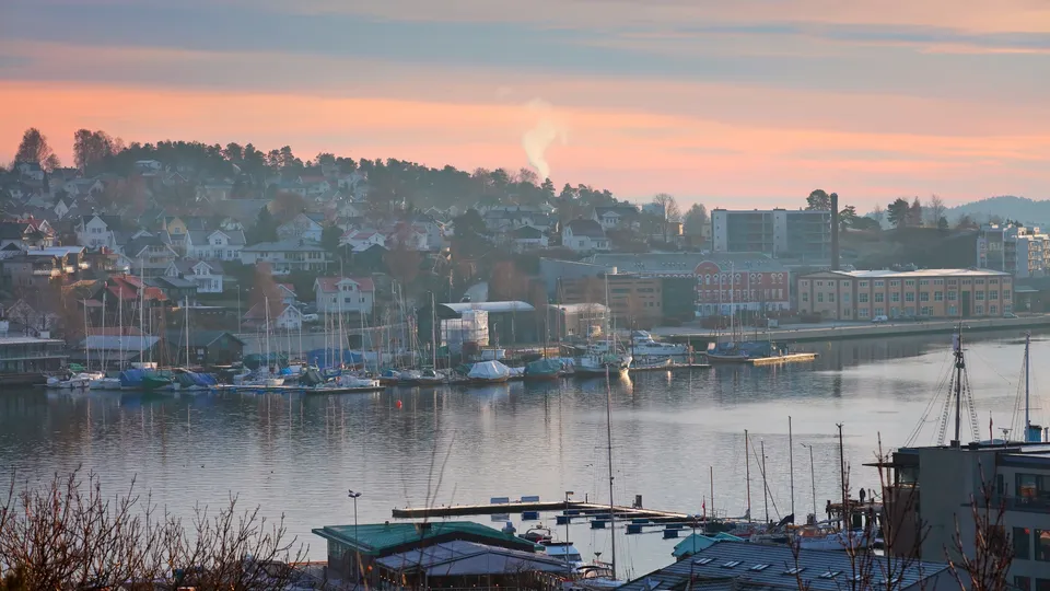 Seilbåter fortøyd i havn i Sandefjord med soloppgang bak hus på åsen.