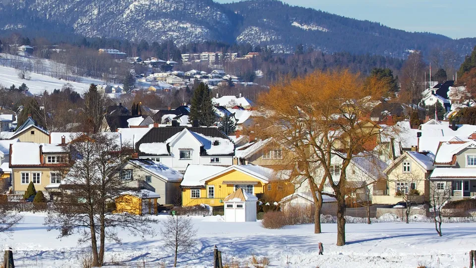 Snøtillagt landsby med fargede hus og snødekte fjell i bakgrunnen.