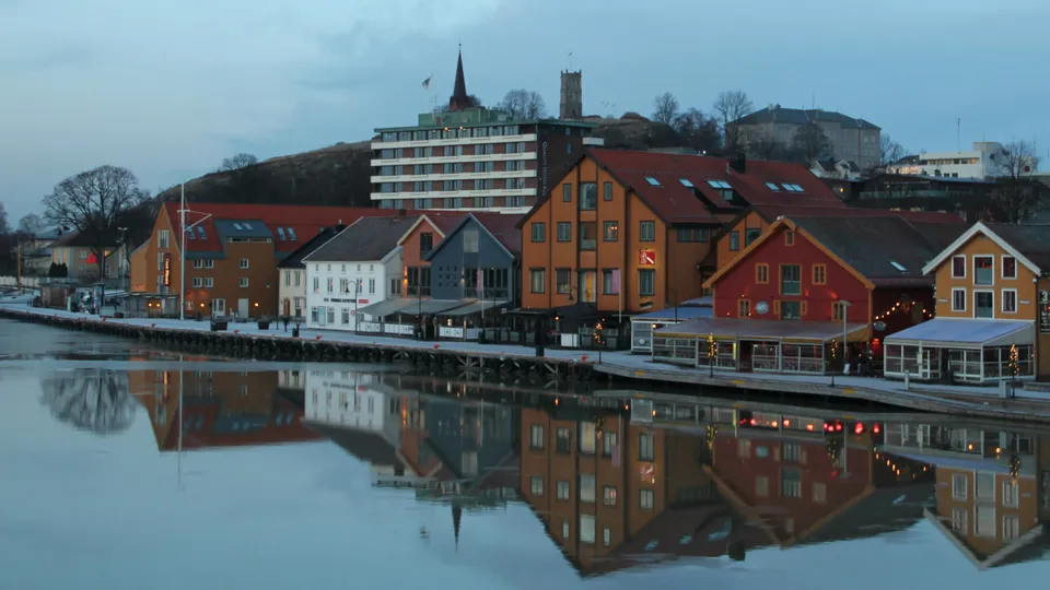 Fargerike bygninger ved vannkanten reflektert i stille vann ved skumring.