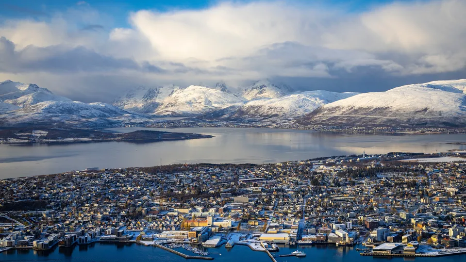 Luftfoto av Tromsø by med snødekte fjell og fjord.
