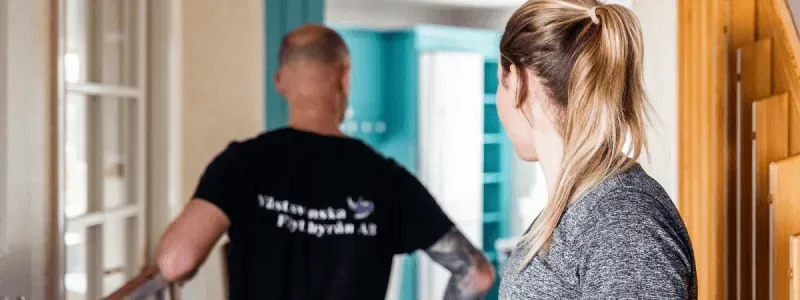 Person står i hallen och ser på medan en flyttfirma bär möbler in i ett hem.