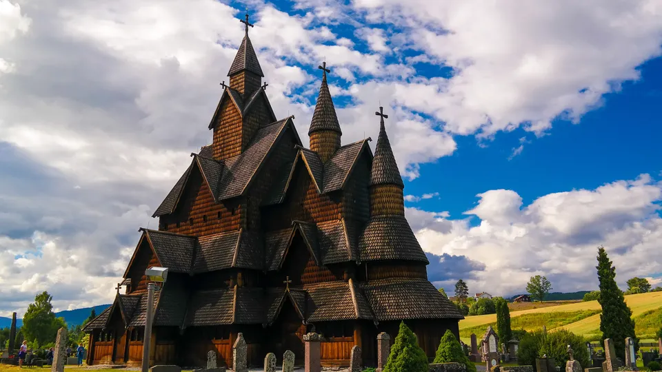 Prydelig stavkirke av tre med flere spir og kors mot skyet himmel.