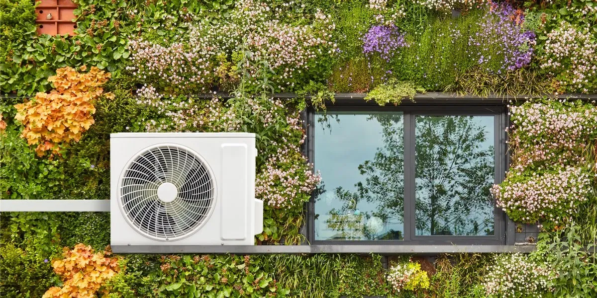 Air conditioning unit mounted on living green wall with flowering plants.