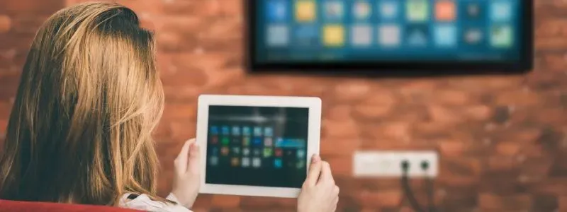 Kvinde i en stol med tablet i hænderne foran et fjernsyn.