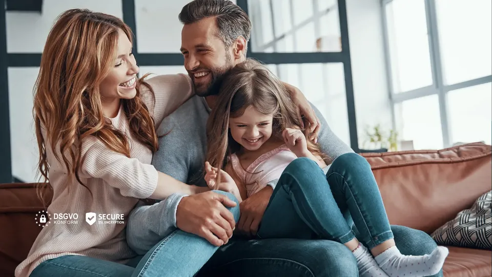 Lachende Familie mit Kind sitzt gemeinsam auf einem Sofa.